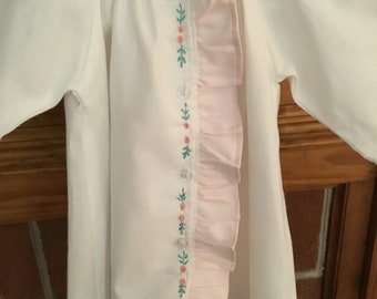 May include: White baby gown with long sleeves and a pink ruffle down the side. The gown has green and pink embroidered leaves and flowers.