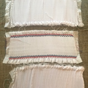 May include: Three white fabric strips with ruffled edges. The middle strip has a red, blue, and white zig-zag pattern.