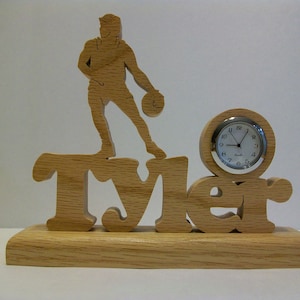 May include: Wooden clock with a carved silhouette of a person playing basketball. The clock face is white with black numbers and hands. The name "Tyler" is carved into the base of the clock.