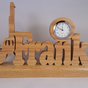 Puede incluir: Un reloj de madera con el nombre "Frank" tallado en él. El reloj está sobre una base de madera y tiene una esfera plateada con agujas negras.