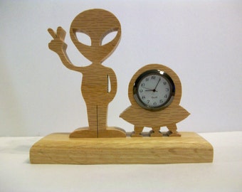 Alien Desk Clock, Alien, giving the peace sign, standing next to an UFO. Clock is battery operated.