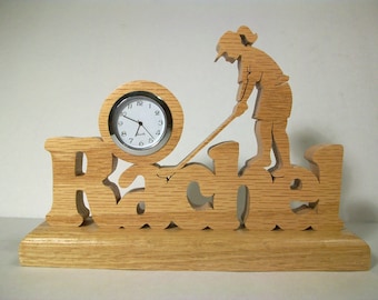 May include: Wooden clock with a golfer silhouette and the name "Rachel" carved into the base. The clock face is white with black numbers and hands.