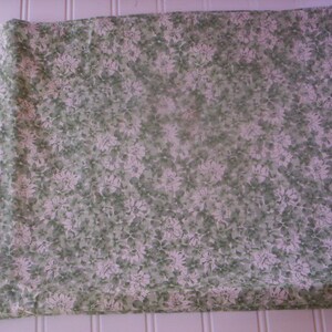 May include: A white fabric with a green floral pattern. The fabric is folded in half and has a smooth texture.