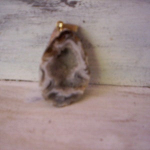 May include: A natural agate pendant with a white and gray pattern. The pendant has a gold-colored bail.