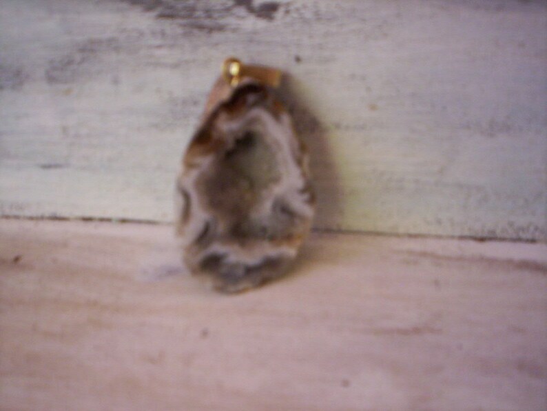 May include: A natural agate pendant with a white and gray pattern. The pendant has a gold-colored bail.