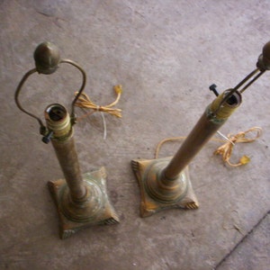 May include: Two gold table lamps with ornate bases and a simple design. The lamps are turned off and the cords are visible.