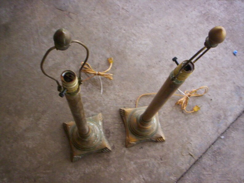 May include: Two gold table lamps with ornate bases and a simple design. The lamps are turned off and the cords are visible.