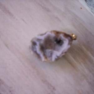 May include: A white and brown agate geode with a gold-colored metal loop attached.