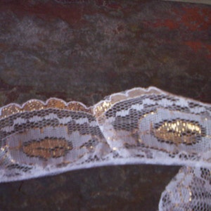 Puede incluir: Borde de encaje blanco con detalles dorados. El encaje tiene un delicado patrón floral.