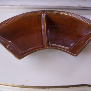 May include: A brown ceramic divided serving dish with a fan-shaped design. The dish has two sections and a smooth, glossy finish.
