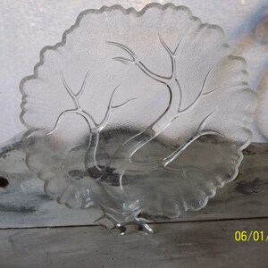 Puede incluir: Plato de servir de vidrio transparente con un dise&ntilde;o de &aacute;rbol. El plato tiene un borde festoneado y una base elevada.