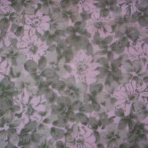 May include: A white fabric with a repeating pattern of green floral designs. The flowers are stylised and have a watercolour effect.