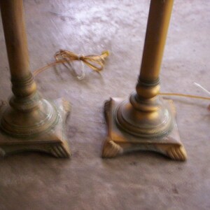 May include: Two gold-toned metal table lamps with ornate bases. The lamps have a vintage style and are in good condition.