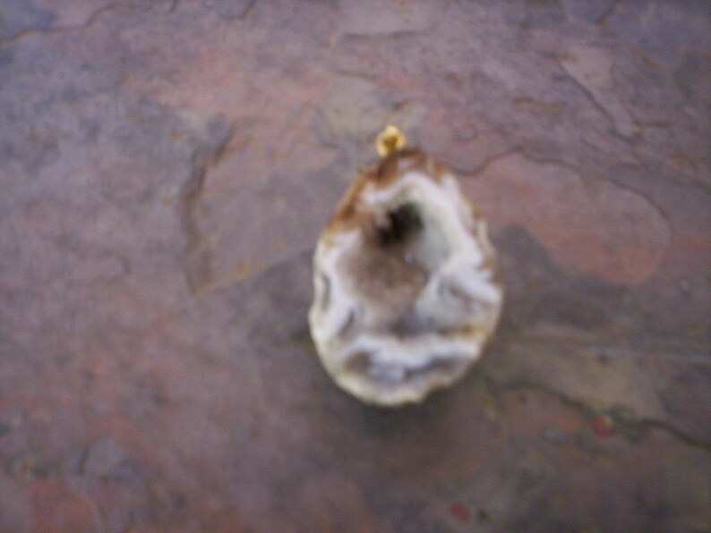May include: A white and brown agate geode pendant with a gold-colored bail.