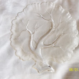 Puede incluir: Un plato de servir de vidrio transparente con forma de &aacute;rbol y borde festoneado. El plato tiene un dise&ntilde;o en relieve de ramas y hojas.