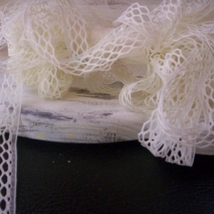 May include: White lace trim with a delicate diamond pattern. The lace is arranged in a loose, flowing style, creating a soft and romantic look.