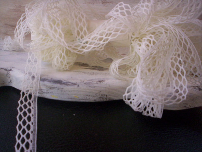 May include: White lace trim with a delicate diamond pattern. The lace is arranged in a loose, flowing style, creating a soft and romantic look.