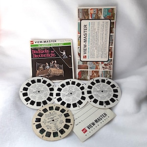 May include: Three View-Master reels for the Bedknobs and Broomsticks movie. The reels are white with black text and images. The text on the reels reads "Walt Disney Productions Bedknobs and Broomsticks". There is a white card with the text "View-Master Picture Reels" and a larger card with the text "View-Master Full-Color 3-Dimensional Pictures".
