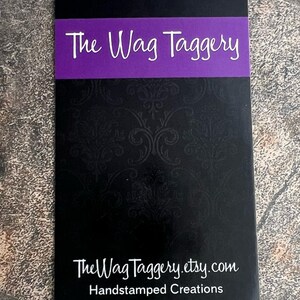 May include: Black business card with a purple banner that reads "The Wag Taggery". The text "TheWagTaggery.etsy.com" and "Handstamped Creations" are printed in white below the banner.