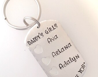 Puede incluir: Llavero de plata con el texto "Daddy's Girls" y tres nombres: Ava, Arianna y Adalyn. El llavero también tiene tres recortes en forma de corazón y el texto "We Love You."