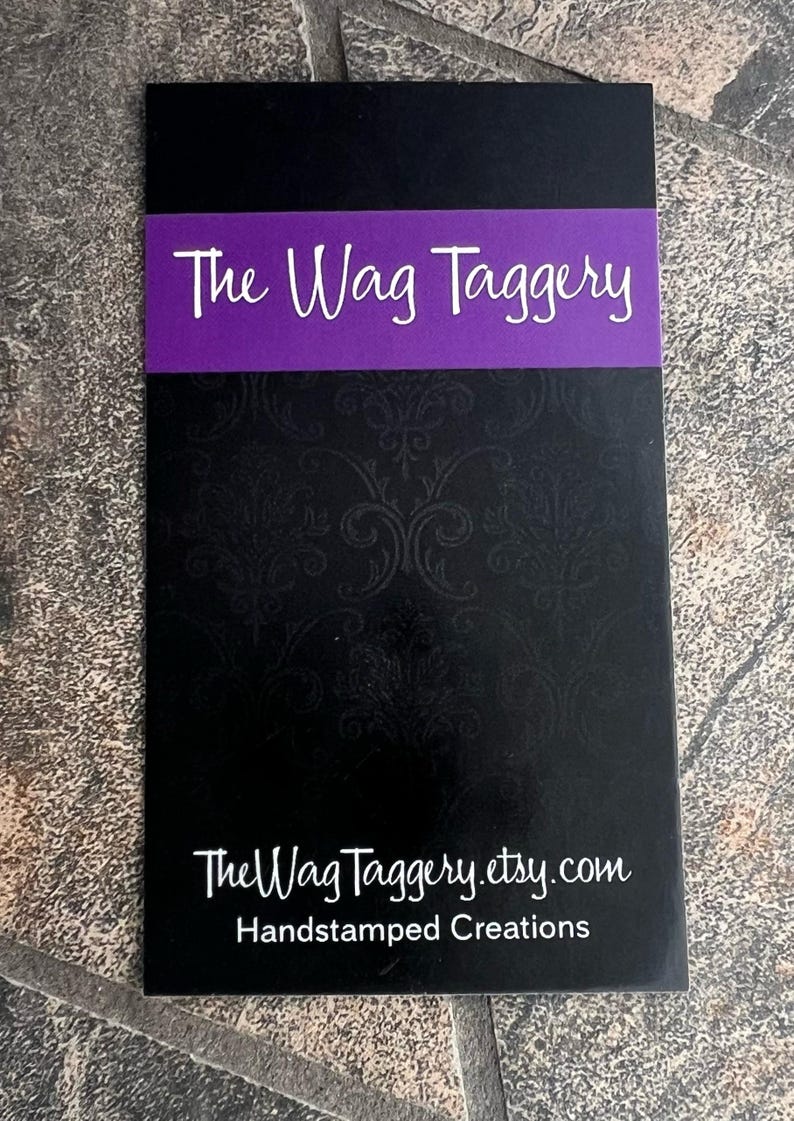 May include: Black business card with a purple banner that reads "The Wag Taggery". The text "TheWagTaggery.etsy.com" and "Handstamped Creations" are printed in white below the banner.