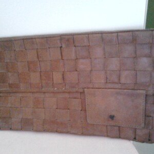 May include: A brown leather clutch bag with a woven pattern. The bag has a small flap pocket on the front.