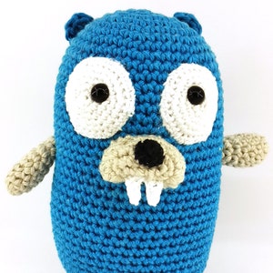 Könnte beinhalten: Ein gehäkeltes blaues und beiges Go-Gopher Plüschtier. Das Spielzeug hat eine schwarze Nase, weiße Zähne und schwarze Augen mit weißen Pupillen.
