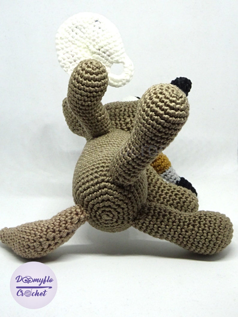 Puede incluir: Un juguete de perro de crochet marr&oacute;n que sostiene una taza de crochet blanca. El perro est&aacute; sentado sobre una superficie blanca.