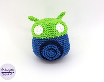Puede incluir: Un juguete de peluche de crochet verde y azul con forma de robot con ojos blancos.