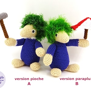 May include: Two crocheted plush toys, one holding a pickaxe and the other holding a red and white umbrella. The toys are both blue and beige with green hair. The text "version pioche A" and "version parapluie B" is below the toys.