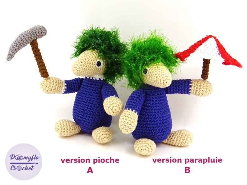 May include: Two crocheted plush toys, one holding a pickaxe and the other holding a red and white umbrella. The toys are both blue and beige with green hair. The text "version pioche A" and "version parapluie B" is below the toys.