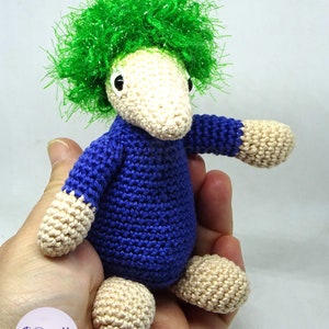 May include: A crocheted stuffed toy with a green fuzzy hair, blue body, and beige legs and arms.