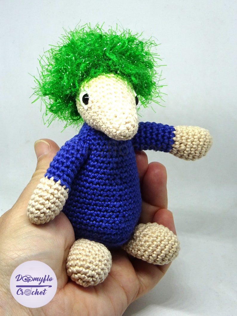 May include: A crocheted stuffed toy with a green fuzzy hair, blue body, and beige legs and arms.