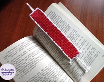 Puede incluir: Un marcapáginas de ganchillo rojo y blanco con forma de jeringa. El marcapáginas está abierto sobre un libro.