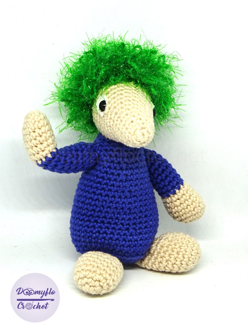 May include: A crocheted plush toy with a blue body, beige legs and arms, and a green fluffy hairdo.