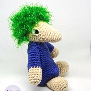 May include: A crocheted stuffed animal with a long snout, blue body, and green hair. The animal is sitting with its legs crossed.
