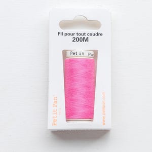 May include: A spool of bright pink sewing thread in a white cardboard package. The packaging features the text Fil pour tout coudre 200M, Petit Pan Paris, and the website www.petitpan.com. The spool label reads Petit Pan.