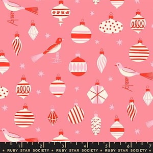 May include: A pink fabric featuring a repeating pattern of white and red Christmas ornaments and birds, interspersed with small white stars. A black ruler at the bottom displays measurements in inches, labeled Ruby Star Society.
