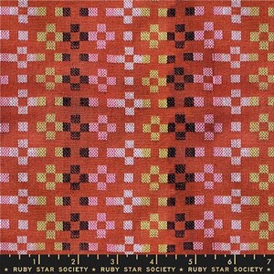 May include: Close-up of a fabric with a repeating pattern of cross-shaped designs. The pattern features squares in black, white, pink, and yellow on a reddish-orange background. The text "RUBY STAR SOCIETY" is at the bottom.