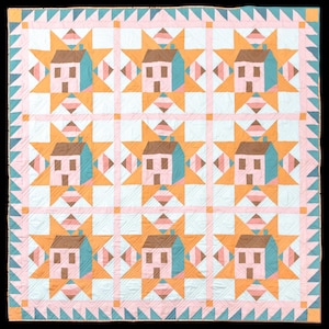 May include: A handmade quilt featuring a repeating pattern of houses and starbursts. The houses are pink with teal roofs, set against a background of white and orange starbursts. The quilt is bordered with a pink and teal triangle pattern.