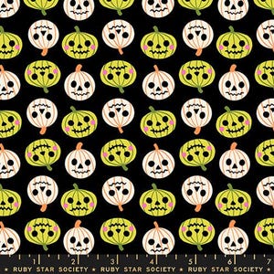 Peut inclure: Un tissu noir avec un motif répétitif de citrouilles d'Halloween stylisées en vert citron et blanc. Chaque citrouille présente un visage sculpté unique avec des joues roses. Une règle en bas indique 18 cm, avec le texte Ruby Star Society.