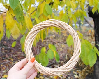 May include: A circular wreath base constructed from light beige, natural woven willow branches. The structure consists of multiple thin, flexible twigs intertwined to form a sturdy, hollow ring shape with a textured, organic appearance.