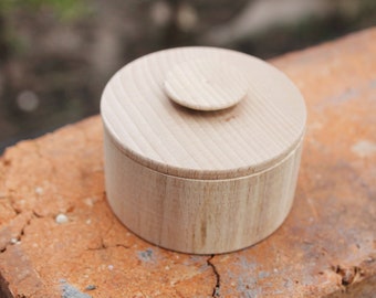 May include: A round wooden box with a lid. The box is made of light wood and has a smooth finish.