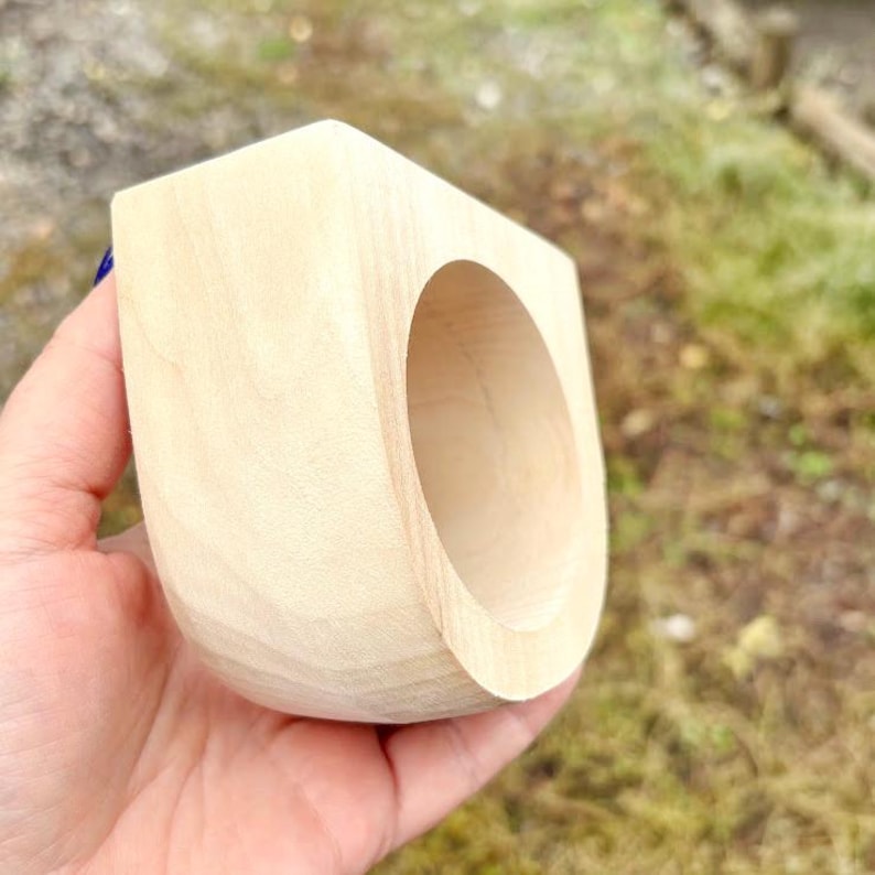 May include: A light-colored, unfinished wooden ring with a thick, chunky, and rounded geometric shape. The wood grain is visible across the smooth, sanded surface of the band, which features a large, circular opening in the center.