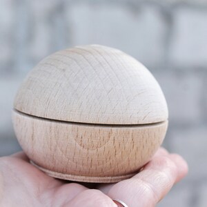 May include: A small, round, wooden box with a lid. The box is made of light wood and has a smooth finish.