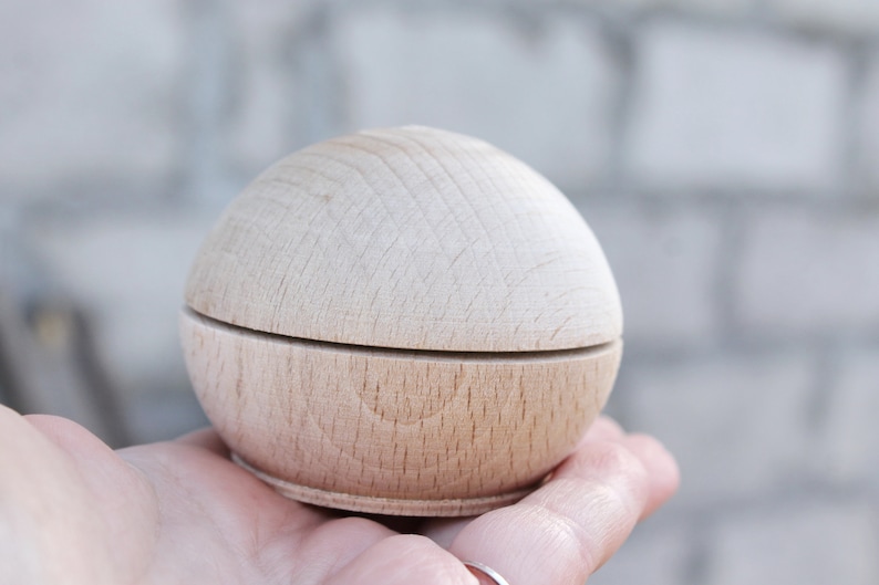 May include: A small, round, wooden box with a lid. The box is made of light wood and has a smooth finish.