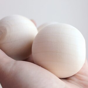 May include: Three smooth, white wooden balls in a hand. The balls are round and have a slightly textured surface.
