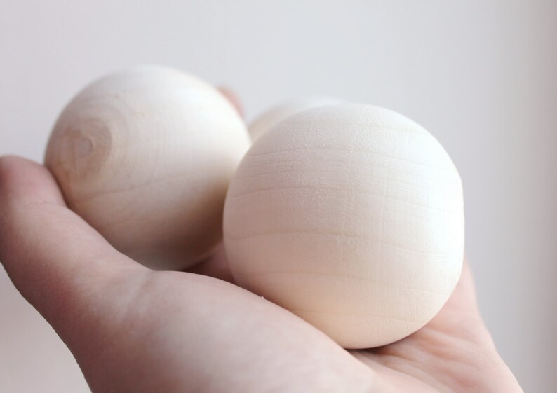 May include: Three smooth, white wooden balls in a hand. The balls are round and have a slightly textured surface.