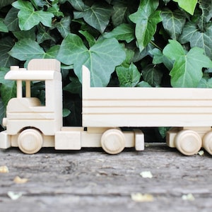 May include: A wooden toy truck with a flatbed trailer. The truck is unpainted and has a simple design.