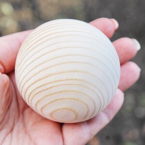 Puede incluir: Primer plano de una bola de madera blanca con c&iacute;rculos conc&eacute;ntricos tallados en la superficie. La bola est&aacute; siendo sostenida en la mano de una persona.